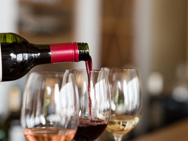 Pouring red wine from bottle into the wineglass on bar. Close up of red wine pouring from bottle to glass in a winery. Wine tasting in a winehouse.